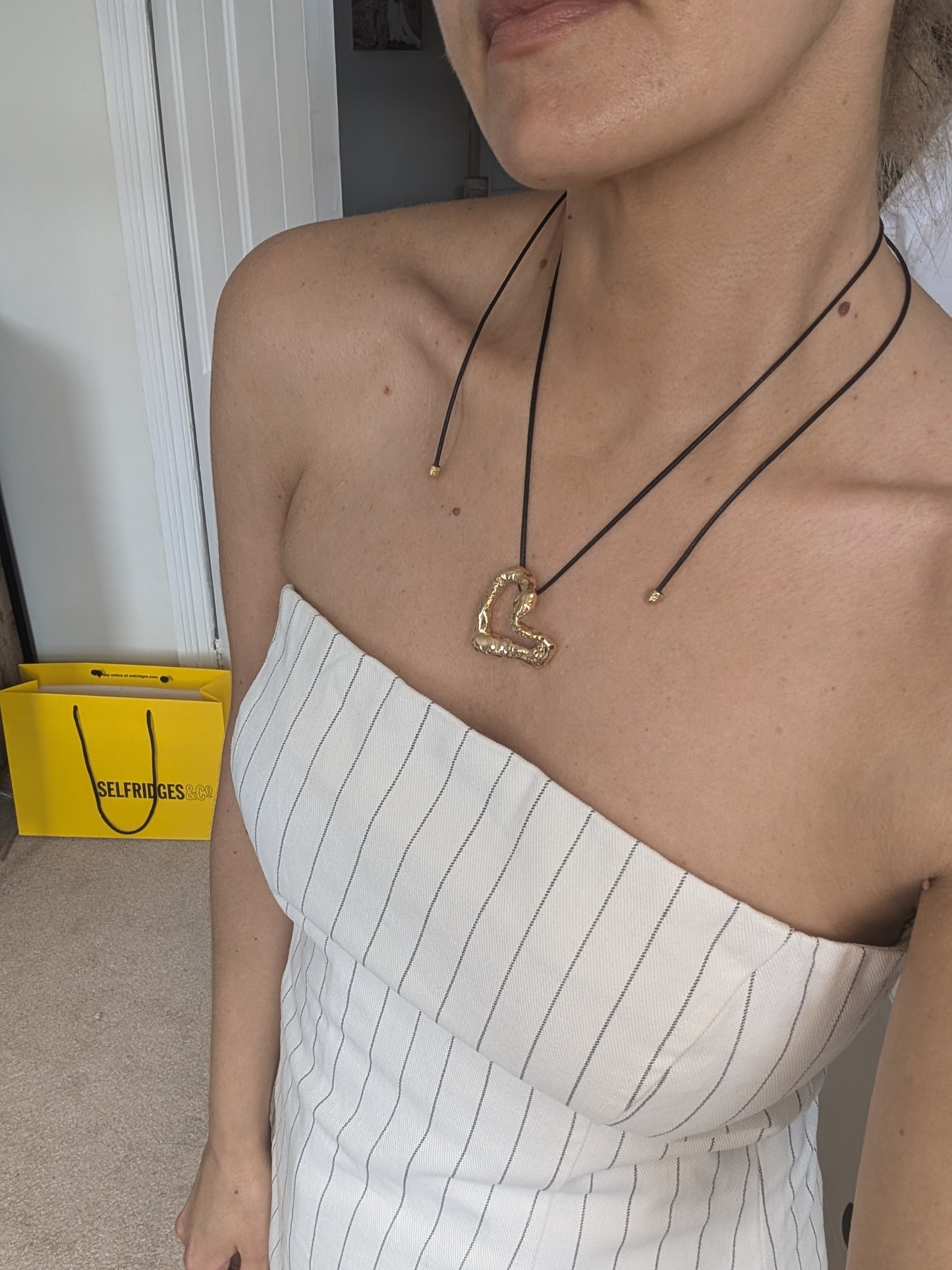 Person wearing a gold necklace with a heart pendant, standing indoors.