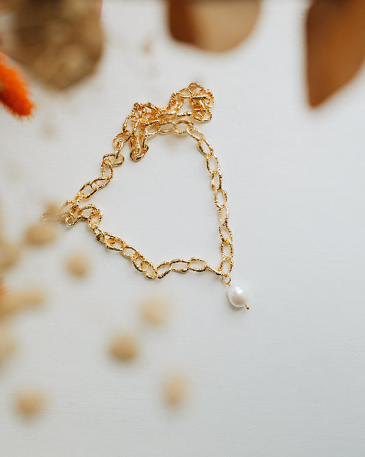 A chunky chain necklace with pearl pendant scattered on a white back ground surrounded by out of focus dried flowers