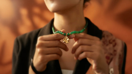 Closeup of green agate Another Mother necklace worn by female model on a warm gold background